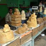 Gur, or Jaggery, is Indian raw sugar. Sugarcane juice (or palm sap) is boiled until it will set up when cooled  in a bucket or other mold. It varies in color, sweetness, and flavor intensity. I found this shop in Udaipur, in Rajasthan.